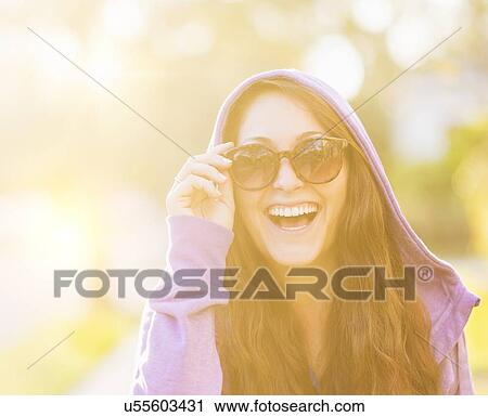 Stock Image - Portrait of smiling woman in hoodie with sunglasses. Fotosearch