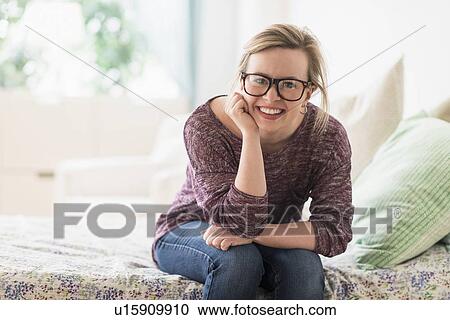 Stock Image - Portrait of smiling young woman sitting on bed. Fotosearch