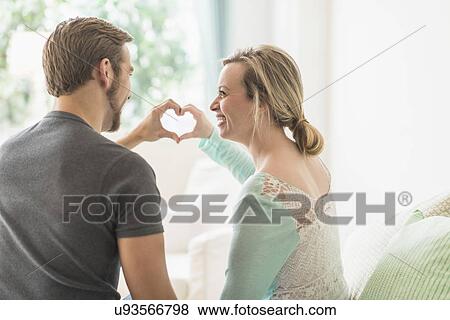 Stock Photo - Rear view of couple making heart shape with hands. Fotosearch