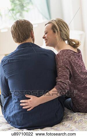 Rear view of young couple sitting on bed View Large Photo Image Stock Image - Rear view of young couple sitting on bed. Fotosearch