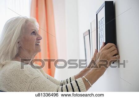 Senior woman hanging picture frame on wall View Large Photo Image Stock Photograph - Senior woman hanging picture frame on wall. Fotosearch