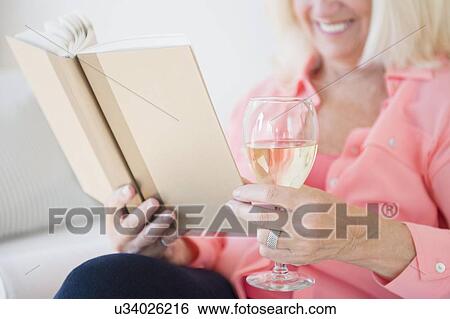 Stock Photograph - Senior woman reading book and drinking wine. Fotosearch