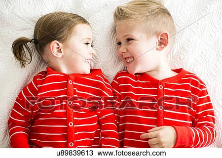 Stock Image - "Siblings (2-3, 4-5) in red pajamas lying on bed". Fotosearch