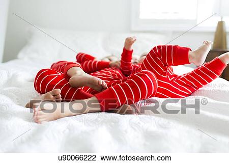 Stock Image - "Siblings (2-3, 4-5) in red pajamas lying on bed". Fotosearch