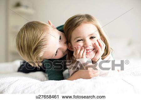 Stock Image - "Siblings (2-3, 4-5) whispering in bedroom". Fotosearch