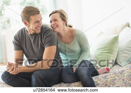 Smiling couple sitting on bed View Large Photo Image Picture - Smiling couple sitting on bed. Fotosearch