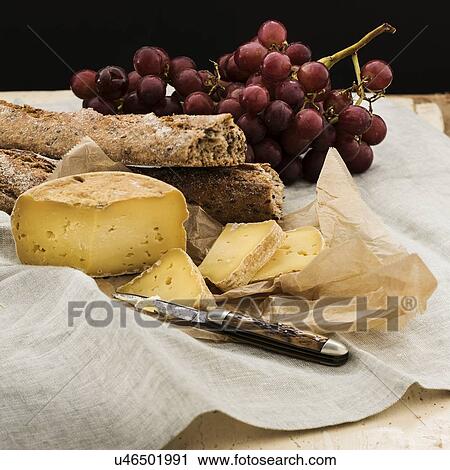 Stock Image - "Still life with grapes and cheese and bread slices on wooden table, studio shot". Fotosearch