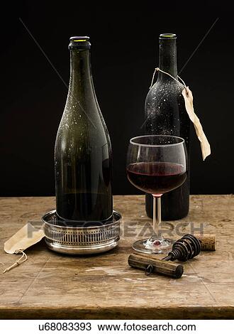 Stock Image - "Still life with red wine glass and bottles on wooden table, studio shot". Fotosearch