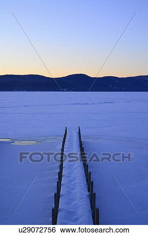 Stock Photograph - "Symmetrical image of snowed jetty with footprints at dawn, hills on horizon". Fotosearch