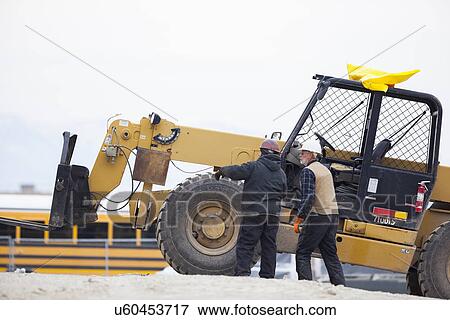 Stock Photo - Two men standing next to earthmover. Fotosearch