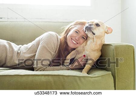 Stock Image - Woman lying on sofa embracing pug. Fotosearch