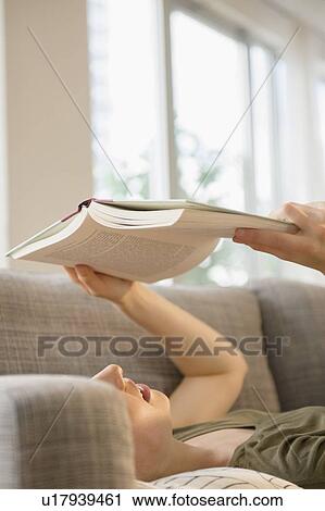 Stock Image - Woman reading book on sofa. Fotosearch