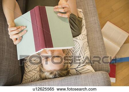 Stock Photography - Woman reading book on sofa. Fotosearch