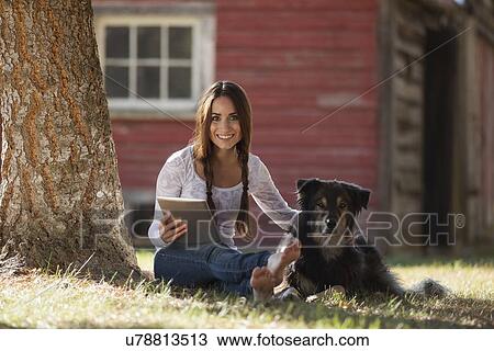 Stock Image - Woman sitting with dog under tree. Fotosearch