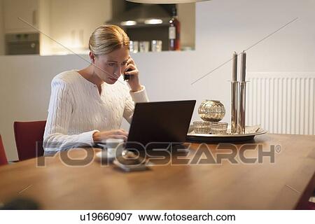 Woman using laptop and cell phone at home View Large Photo Image Stock Photo - Woman using laptop and cell phone at home. Fotosearch