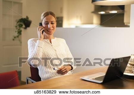 Woman using laptop and cell phone at home View Large Photo Image Stock Photo - Woman using laptop and cell phone at home. Fotosearch