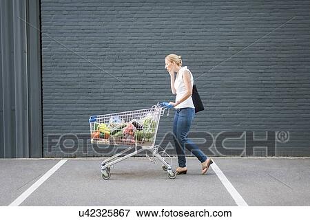 Stock Photo - Woman walking with shopping cart. Fotosearch