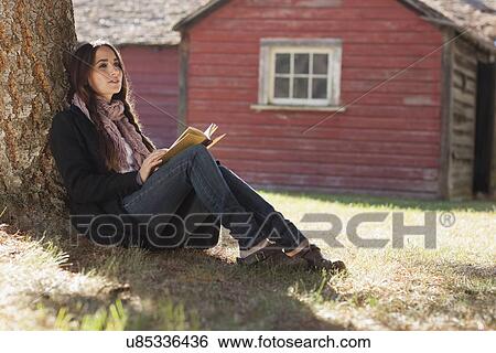 Stock Photograph - Woman with book sitting under tree. Fotosearch