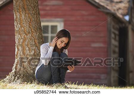 Woman with tablet sitting under tree View Large Photo Image Picture - Woman with tablet sitting under tree. Fotosearch
