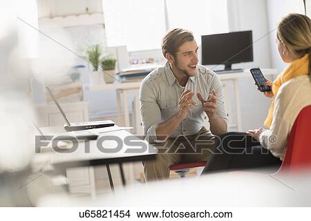 Picture - Young man and woman discussing at desk in office. Fotosearch