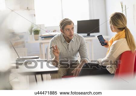 Stock Photography - Young man and woman discussing at desk in office. Fotosearch