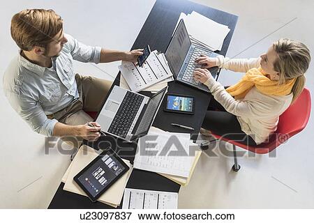 Young man and woman with laptops at desk in office View Large Photo Image Stock Photo - Young man and woman with laptops at desk in office. Fotosearch