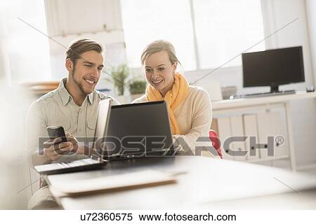 Stock Photography - Young man and woman working together with laptop in office. Fotosearch