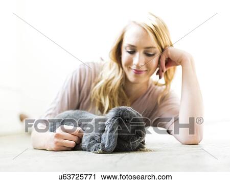 Young woman lying on floor and stroking rabbit View Large Photo Image Stock Image - Young woman lying on floor and stroking rabbit. Fotosearch