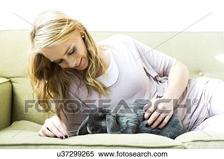 Stock Photography - Young woman lying on sofa stroking rabbit. Fotosearch