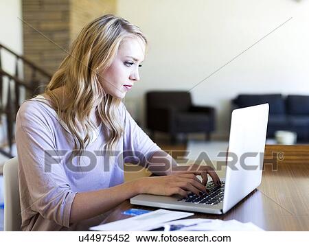 Stock Image - Young woman using laptop at table. Fotosearch