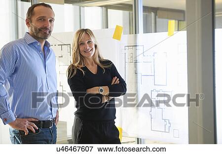 Architects standing by plans on glass wall View Large Photo Image Stock Photo - Architects standing by plans on glass wall. Fotosearch