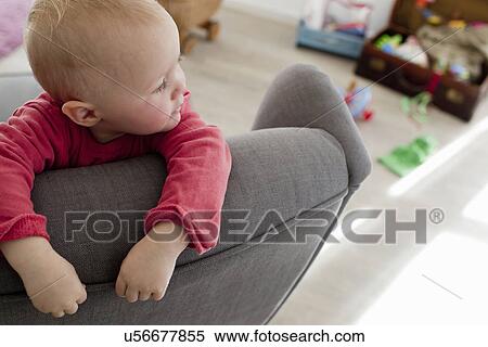 Stock Photography - Baby girl in living room leaning on sofa. Fotosearch