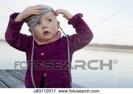 Baby girl on lake pier trying to put on hat View Large Photo Image Stock Photo - Baby girl on lake pier trying to put on hat. Fotosearch