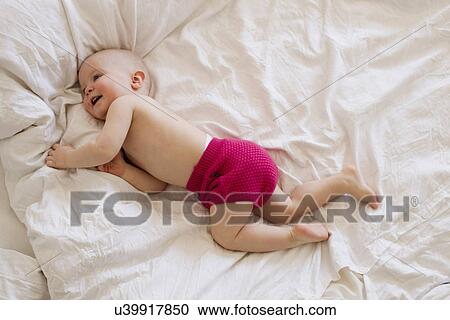 Stock Image - Baby girl rolling and playing on bed. Fotosearch