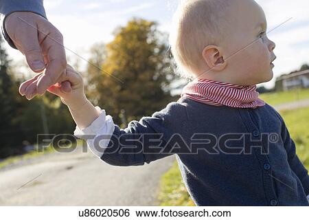 Stock Photograph - Baby girl toddling on rural road holding fathers hand. Fotosearch