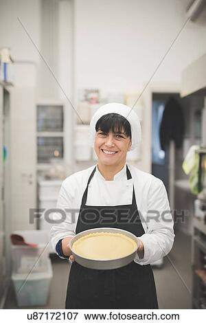 Stock Photo - Baker carrying pan with pie in kitchen. Fotosearch