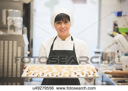 Stock Photograph - Baker carrying tray of pastries in kitchen. Fotosearch