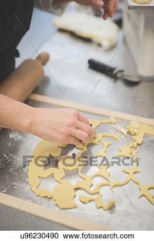 Stock Image - Baker cutting dough with mould in kitchen. Fotosearch