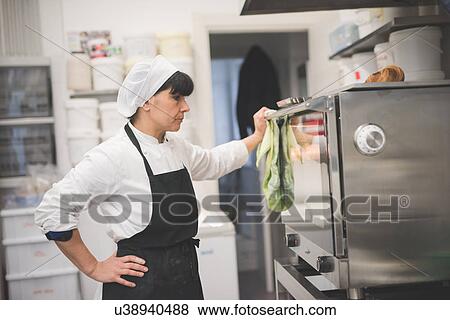 Baker looking into oven in kitchen View Large Photo Image Stock Photo - Baker looking into oven in kitchen. Fotosearch