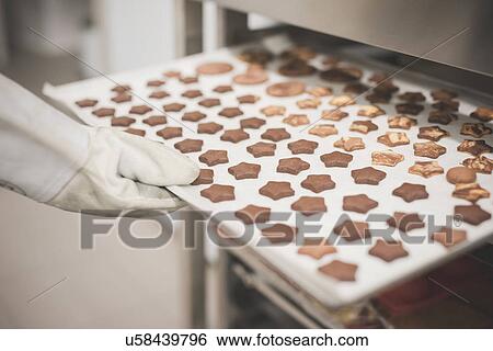 Stock Photograph - Baker placing tray of star-shaped cookies into oven. Fotosearch