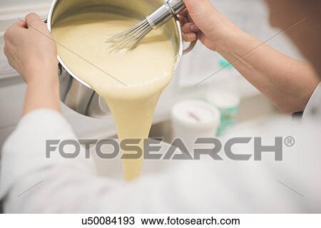Stock Image - Baker pouring mixture into bowl in kitchen. Fotosearch
