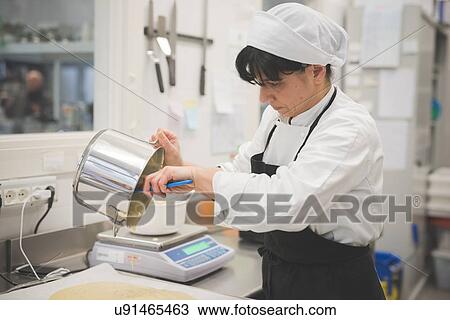Stock Image - Baker pouring mixture onto tray in kitchen. Fotosearch