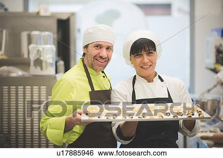 Stock Photograph - Bakers carrying tray of pastries in kitchen. Fotosearch