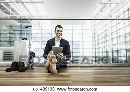 Barefoot businessman in airport departure lounge sitting on floor with digital tablet View Large Photo Image Stock Image - Barefoot businessman in airport departure lounge sitting on floor with digital tablet. Fotosearch