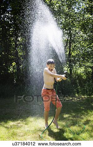 Stock Image - Boy playing with garden hose. Fotosearch