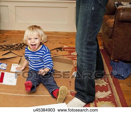 Boy sitting laughing on cardboard box in living room View Large Photo Image Stock Image - Boy sitting laughing on cardboard box in living room. Fotosearch