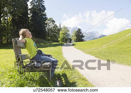 Stock Photo - "Boy sitting on park bench at rural roadside, Eckbauer bei Garmisch, Bavaria, Germany". Fotosearch