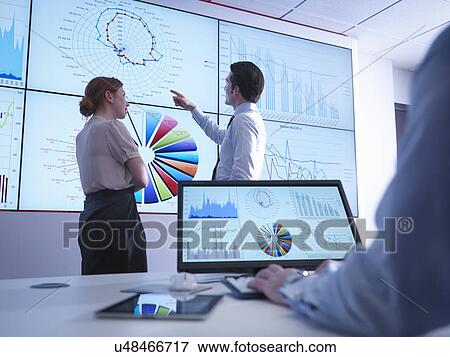 Stock Photo - Business colleagues discussing graphs on screen in meeting room. Fotosearch