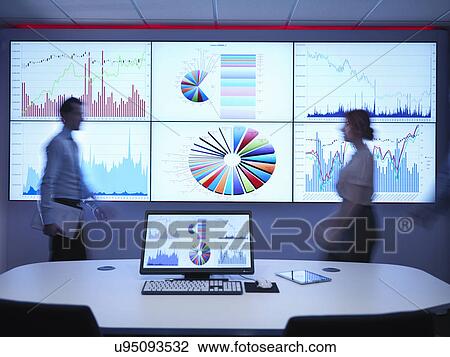 Stock Image - Business people walking in front of graphs on screen. Fotosearch