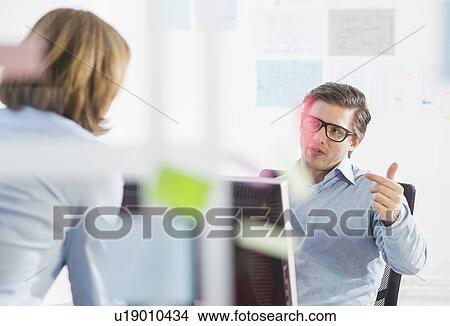 Picture - Businessman and woman chatting at office desk. Fotosearch